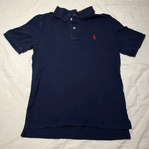 Ralph Lauren pikétröja  - En blå Ralph Lauren pikétröja som är i fint men använt skick. Tröjan e slim så den kan sitta lite tajt på större människor. Annars passar den personer som är mellan 165-175 cm långa. Nypris på tröjan är cirka 900 kr. 