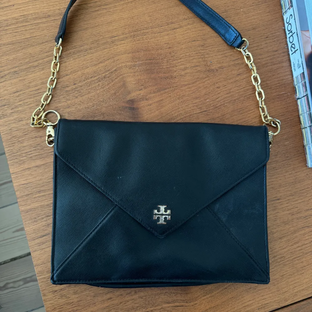 Tory burch clutch i svart med guldetaljer. Lädret är i fint skick men tyvärr är detaljerna lite slitna. . Accessoarer.