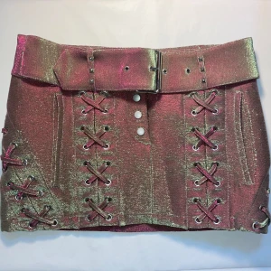 Cool kjol - Jättefin mini-kjol med justerbart bälte och rymliga fickor. Kjolen skiftar i lila/rosa och grönt och den glittrar massa! Midjemått raktöver: 42 cm