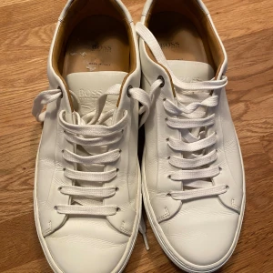 Vita sneakers från Hugo Boss - Ett par vita sneakers från Hugo Boss, tillverkade i Italien. Skorna har snörning och är gjorda av skinn. Knappt använda 