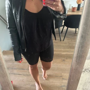 Svart skinnjacka - En svart skinnjacka med dragkedja framtill och två dragkedjeförsedda fickor. Jackan har långa ärmar och detaljer som spännen på sidorna och quiltade partier på axlarna.