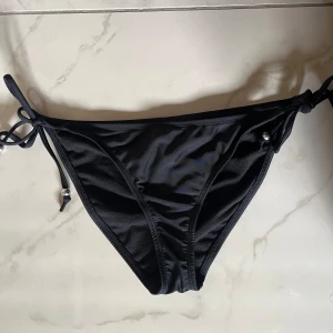 Svart bikiniunderdel - Svarta bikinitrosor från Nly beach. Har en scrunch detalj bak som framhäver rumpan. Fint skick. Säljer även en topp från Nly beach med liknande pärlor.