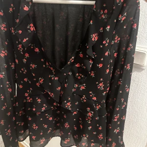 Somrig  - En svart tröja med blommor på, tät runt midja, öppen runt bröstkorgen. 