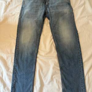 Ett par blå jeans från Replay i storlek 30. Jeansen har en klassisk design med fem fickor och en knappgylf. De är tillverkade i bomull och har en lätt slitning på framsidan för en avslappnad look. Använd några fåtal gånger, i nyskick!