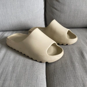 Yeezy slides / tofflor - Säljer ett par yeezy slides i storlek 45. Färgen är beige. Vissa små rynklor men inget man märker av. 9/10 använd nån gång annars helt ny. Skriv för mer info