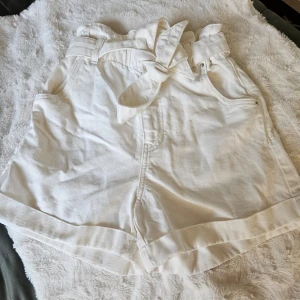 Högmidjade jeansshorts nytt - Vita högmidjade shorts med tillhörande skärp,dragkedja och knappar på shortsen och det är även resår i midjan. Fickor bak och fram. Strl 36. Katt finns I hemmet