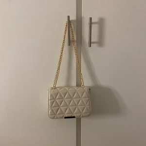 Väska från glitter - Beige väska med guldiga detaljer från glitter, helt oanvänd. Axelbandet går att ha långt eller kort. Nypris 299kr Fler bilder går att få om man vill😊