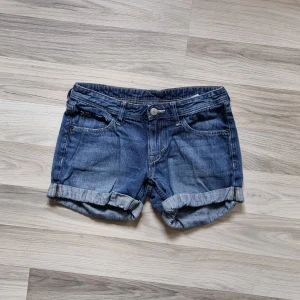 Blå jeansshorts - Ett par blå jeansshorts med upprullade ben. Shortsen har fram- och bakfickor samt en knapp och dragkedja framtill.