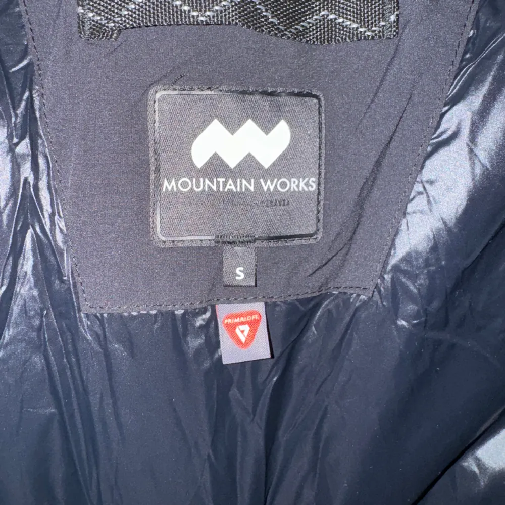 Dunjacka från Mountain works.  Storlek: S Material: Polyester Helt ny, men utan prislapp.  Kommentar från säljaren: Dunväst från Mountain Works med primaloft stoppning. Dragsko i midjan.. Jackor.