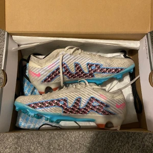 Fotbollsskor - Nike Air Zoom Mercurial Vapor 15 Elite FG Blast - Vit/Blå/Rosa/Indigo Haze. Storlek 42,5. Skick 8/10. Nypris 3149kr Säljer eftersom de har blivit för små. Får påse med i köpet. Skriv för mer bilder.
