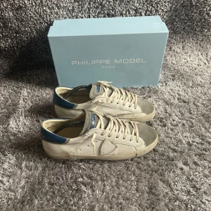 Philippe Model sneakers -  Philippe Model skor i vit och grå färg med blå detaljer. Box och dustbag medföljer. Skick: 8/10, Sulan har släppt lite på ca 2 cm lång sträcka på ena skon men utöver det är skicket fint!Storlek: 42. Kontakta oss för fler bilder eller info!🤗