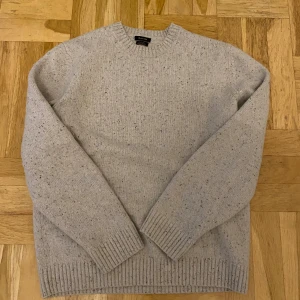 Stickad Ull tröja från Massimo Dutti - En beige stickad ull tröja från Massimo Dutti med ett diskret melerat mönster. Tröjan har långa ärmar och ribbstickade muddar vid ärmslut, hals och nederkant.