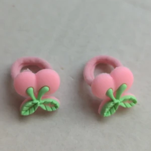 Rosa örhängen med körsbärsdesign - Ett par söta rosa hårklämmör med en design som liknar körsbär. hårklämmör har två rosa bär och gröna blad, vilket ger dem ett lekfullt och färgglatt utseende.
