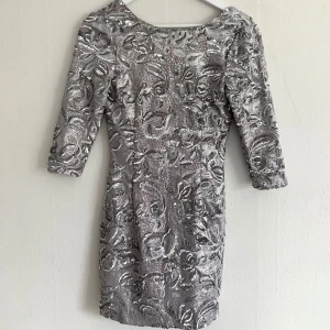 Silvrig paljettklänning med låg rygg - Dragkedja i ryggen.