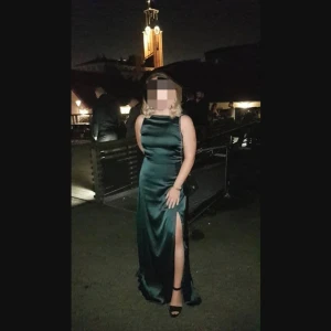 Klänning  - Fin aftonklänning i mörkgrön färg. Öppning i ryggen med vacker spetskant som detalj. Slits framtill. Använd 1 gång.