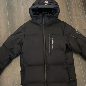Sail Racing Vinterjacka - Sail Racing Jacka i storlek S, men passar bra som M. Dragkedjan har byts ut och snöret på jackans ena snörstopp har gått av. Annars är jackan perfekt!