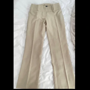 Lågmidjade kostymbyxor  - Oanvända kostymbyxor som är i beige sandfärg och linneaktigt material.   Midja : 37cm  Längd hela : 99cm  Innerbenslängd: 80.5cm