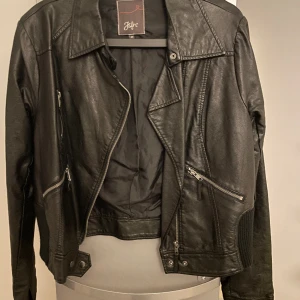 Skinnjacka fejk  - Fejk skinnjacka i storlek 44. Märket jsfn.  Mudd i midjan dekorativt på sidorna nertill 