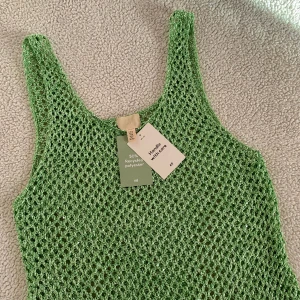 H&M grön glittrig virkad klänning - Otroligt snygg grön virkad klänning från H&M med glitter. Det är svårt att fånga denna skönhet på bild, den glittrar mycket mer i verkligheten nämligen. Ny med tags kvar. Storlek M men tycker den är nice OZ på mig som är S. Perfekt till semestern!