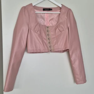 Rosa topp  - Den är helt oanvänd i toppen skick! Materialet är skinn/läder (ej riktig). Det finns en dold dragkedja där bak, där fram knäppningar. 