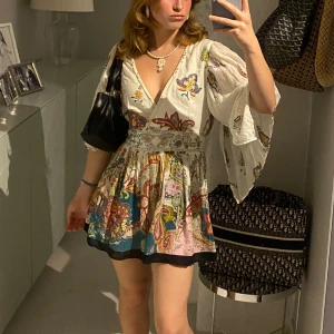 Vit kortklänning med blommigt mönster - Säljer en superfin vit kortklänning med ett färgglatt blommigt mönster. Klänningen har en djup v-ringning och vida trekvartsärmar. Perfekt för sommarens alla fester! 🌸KLICKA INTE KÖP INNAN NI SKRIVIT MED MIG💕