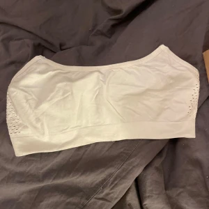 Vit axelbandslös topp - Säljer en vit axelbands topp som är perfekt för sommaren. Den är tillverkad i ett mjukt och stretchigt material som gör den bekväm att bära. Toppen har en enkel design med små hål på sidorna för extra ventilation. 