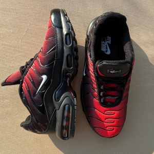 Nike Air Max Plus TN - Ett par Nike Air Max Plus TN sneakers i svart och röd färg. Skorna har en synlig Air Max-enhet i sulan och en vit Nike-logotyp på sidan. Helt nya som jag fick i en bortappad post som jag köpte.  Deadpool 
