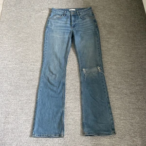 Blå jeans från Perfect Jeans - Säljer ett par blå jeans från Gina Tricot i storlek 36. De är bootcut jeans som har ett hål på ena benet vilket ger dem en cool och avslappnad look. Perfekta för vardagsbruk! 