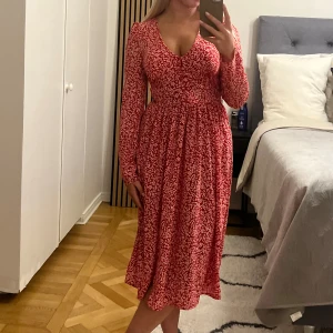 Röd blommig klänning från Monki - Säljer en superfin röd klänning från Monki med ett blommigt mönster. Klänningen är i storlek 32 men skulle säga att den passar en 34 också 