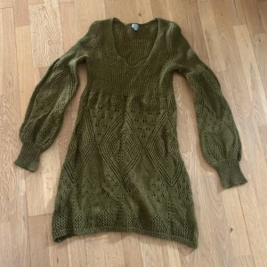 Olivgrön stickad klänning från Index - Säljer en superfin olivgrön stickad klänning från Lindex i storlek M. Klänningen har ett vackert mönster med hålstickning och en v-ringad hals. Den har långa ärmar med ribbade muddar och är perfekt för höst och vinter. Passar både till vardags och fest. Går även att ha över ett par byxor för en 2000-tals stil
