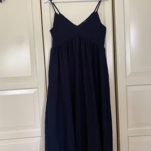Mörkblå ankellång klänning från Vero Moda - Säljer en superfin mörkblå ankellång klänning från Vero Moda. Klänningen har smala axelband och en v-ringad hals. Materialet är lätt och luftigt, perfekt för sommarens fester eller en dag på stranden. Den är i nästintill nyskick och har ett diskret mönster som ger en extra touch. Passar perfekt för både vardag och fest!