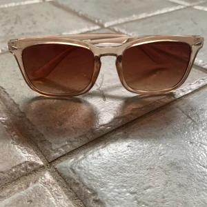 Bruna solglasögon med transparent båge - Säljer ett par snygga solglasögon med bruna linser och transparenta bågar. Perfekta för soliga dagar och ger en cool look. De är i bra skick och passar de flesta ansiktsformer. Perfekta för både vardag och fest!