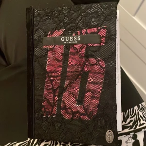 Svart och röd Guess anteckningsbok - Säljer en snygg anteckningsbok, fodralet är gjort av mig själv. Den har en svart spetsöverdrag och en röd bakgrund med ett stort '16' på framsidan. Inuti finns det färgprover och en reklam för Lancôme parfym. Perfekt för att hålla dina anteckningar stiliga och organiserade! eller kan användas som en dagbok eller en skönhetsprovs- dagbok, eller vad du vill.