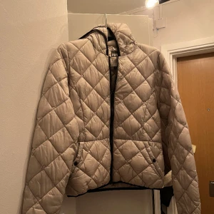 Jacka - Tunn dunjacka. Jackan är lite ljusgrå. Lite trasig på där man hänger upp den, annars utan skråma. Liten i storleken skulle säga att den är mer storleken S.