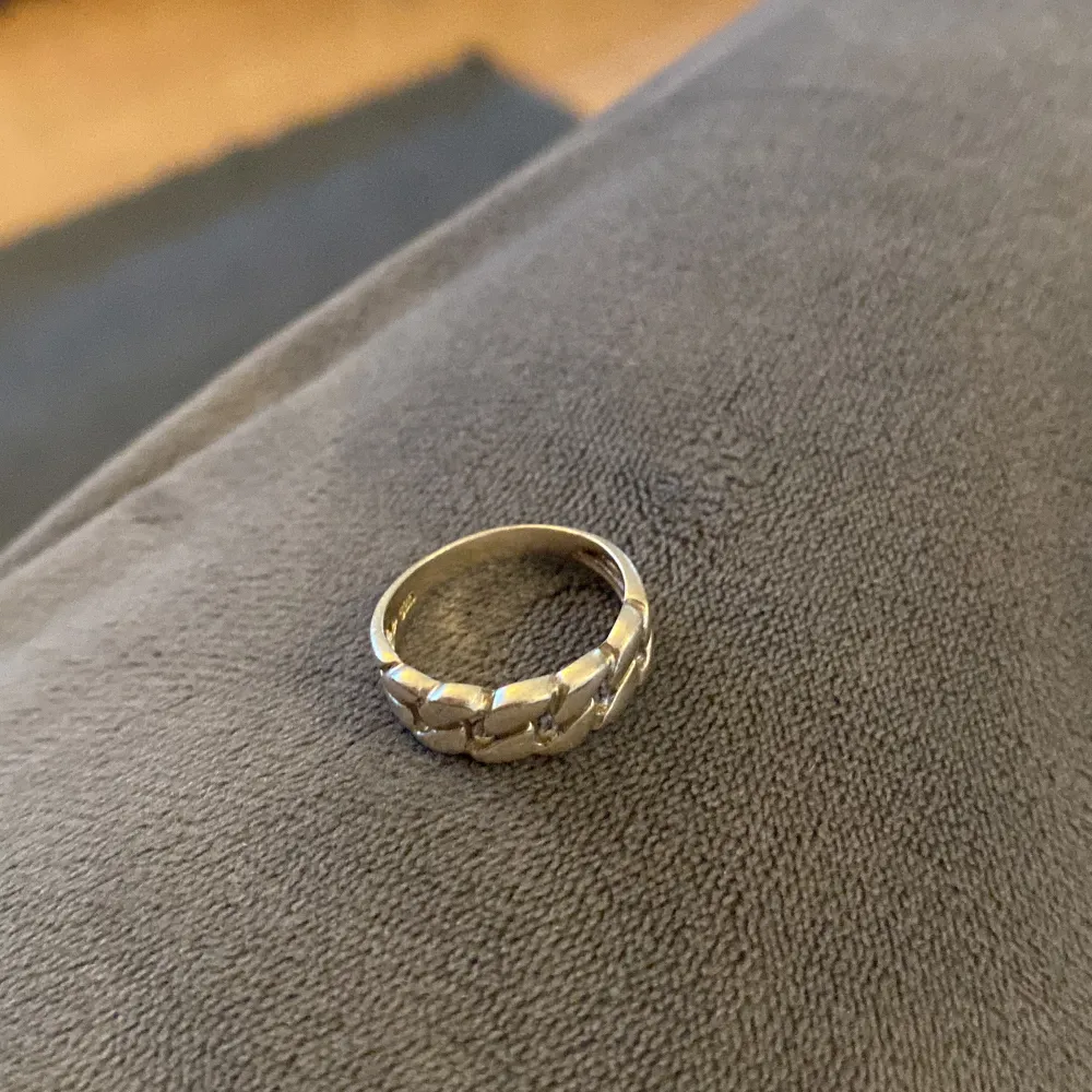 En elegant silverfärgad ring med ett unikt kedjemönster. Ringen har en polerad yta och är designad för att passa både vardagliga och festliga tillfällen.. Asusteet.