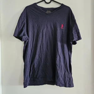 Ralph Lauren t-shirt - Säljer nu en Ralph Lauren T-shirt i färgen marinblå. Loggan är i rött. V-ringad framtill. Köpt på Ralph Lauren. 
