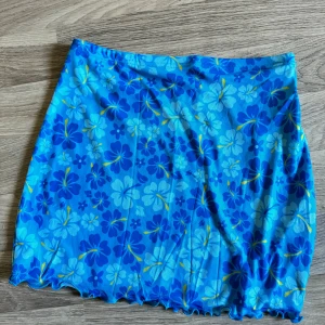 Blå blommig kjol från Shein - En kort blå kjol från Shein med ett blommigt mönster i olika nyanser av blått och inslag av gult. Kjolen har en elastisk midja och är tillverkad i ett lätt och bekvämt material. Innerkjol finns. Mesh utanpå. Endast provad