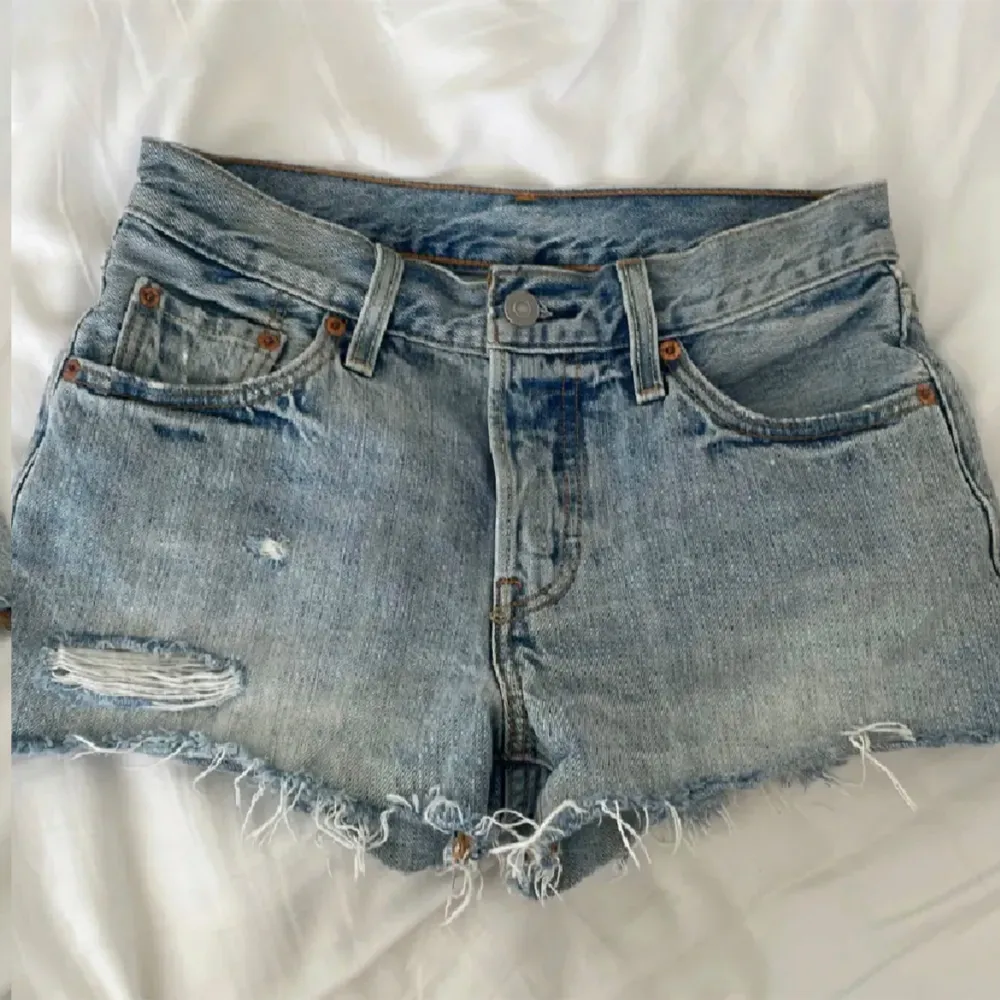 Använd gärna köp nu. Ett par blå jeansshorts från Levi's med slitna detaljer och råa kanter. Shortsen har en knappgylf och fem fickor.. Shorts.