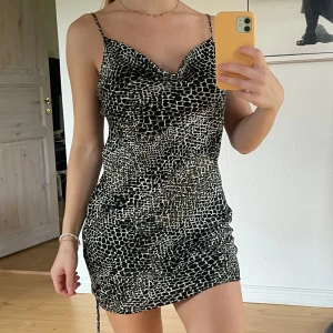 TOPSHOP animal print klänning - Kort ”animal print” klänning från Topshop i satin-material. Knappt använd så är i fint skick. Går att dra upp med bandet på ena sidan som detalj.