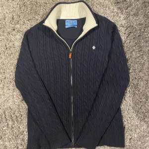 Morris fullzip  - Säljer min skitsnygga Morris fullzip storlek M som är i nyskick. Den är kabelstickad med väldigt mörkblå o vit i insidan och toppkvalitet. Äkta solklart ;) 