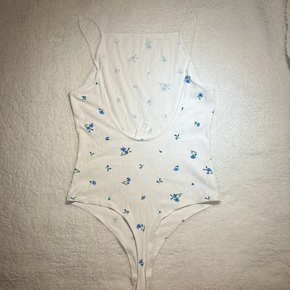 Sommrig vit bodysuit med blå blommor på. Väldigt bra skick och har inte använts mer än ett par gånger och aldrig utan leggings under. Tvättas i 30 grader och är i storlek M. . Toppar.