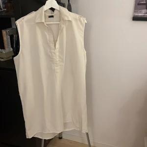 Vit ärmlös skjorta  - En vit ärmlös skjorta i lite tunnare material  Detalj med knapp på axlarna  Halvknäppning Storlek 40