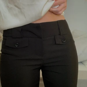 Lågmidjade kostymbyxor  - Lowwaisted kostymbyxor med fina knappdetaljer. Innerbenslängd 67cm. Midjemått 36cm. Ytterbenslängd 90cm