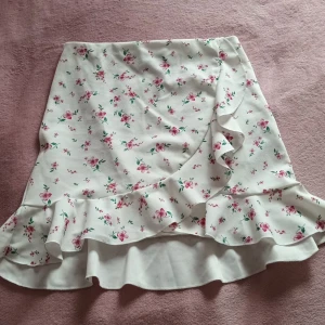 Blommig kjol i strl S från NLY ONE  - En jättevacker sommar dröm till kjol. Den är vit med rosa blommor och gröna blad + en volang. Den är helt oanvänd då jag köpte 2 stycken av misstag men tyvärr tagit bort lappen. Strl S från Nelly