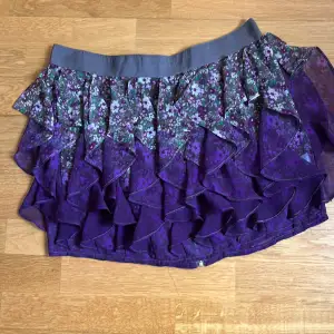 Kort kjol mrd volanger och metall dragkedja på baksidan. Fluffig voluminös festlig kjol cerise/lila med blommig design. 
