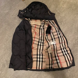 Burberry jacka - Säljer en as fet burberry jacka i storlek S. Den är svart med rutigt mönster och burberry mönster inne i jackan. Jackan är i gott skick men har små defekter. Modellen på annonsen är 185 cm lång och ca 70kg. Passar även M.  Skriv om funderingar!!!