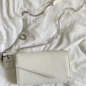 Clutch väska - Säljer denna vita clutch väska, använd en gång är som ny. Bandet som tillkommer är inte använt alls. Ny pris 500kr, mitt pris 259kr + frakt