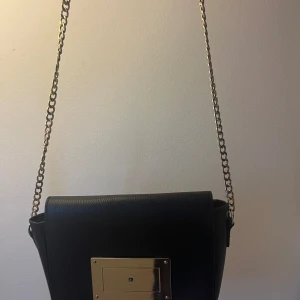 Svart axelväska - Får plats med mobilen och en del andra grejer. En liten bit på frontdelen saknas, men ändå i väldigt bra skick.