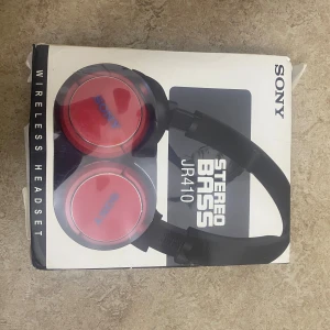 Sony JR410 Wireless Headset - Sony JR410 trådlösa hörlurar med stereo bass, röd färg. Bluetooth 5.3, 40mm högtalare, upp till 15 timmars speltid. Förpackningen har tydliga skador och slitage, men hörlurarna ser nya ut. Perfekt för musik och samtal med kraftfullt ljud.