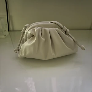 Beige kuvertväska med snörning - Trendig beige kuvertväska i mjukt syntetmaterial med coola snörningsdetaljer på sidorna. Väskan har en puffig, veckad design och stängs med metallspänne. Och aldrig använd💞💞